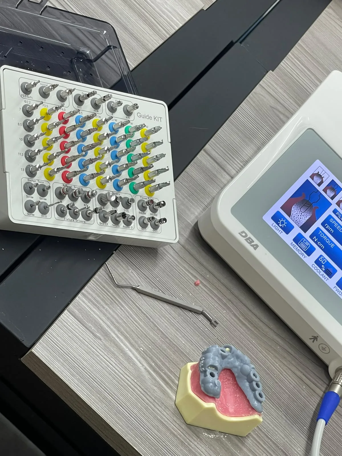 Sobre la mesa del aula: un kit quirúrgico de implantes abierto, un motor de implantes y un modelo de arcada con implantes colocados