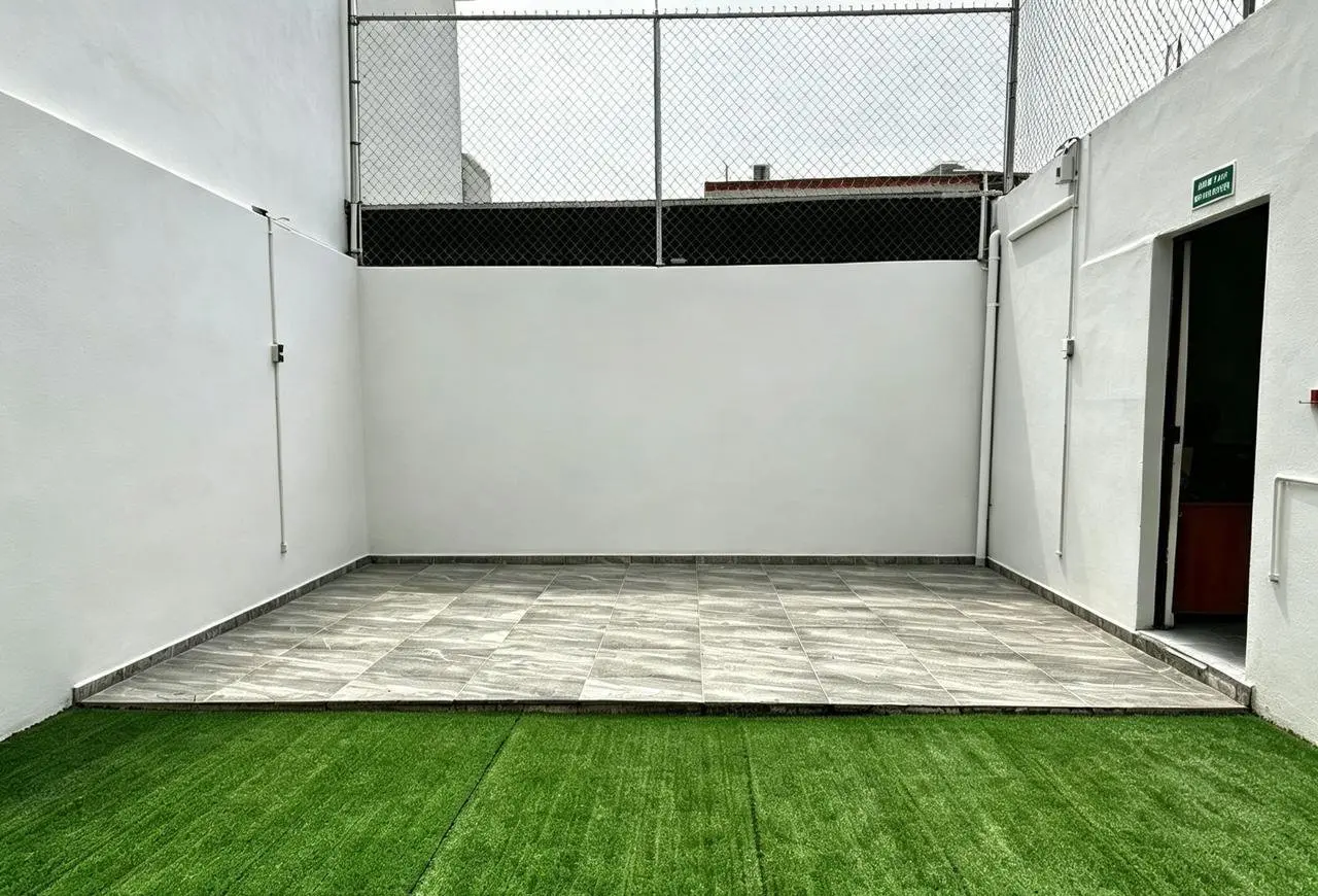 Terraza equipada con una mesa, sombrilla y sillas sobre el pasto sintético